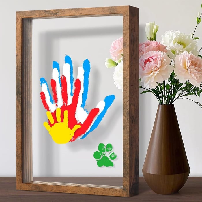 Wood-colored rustic wooden transparent handprint frame with layered blue, red, yellow and green family handprints beside pink flowers