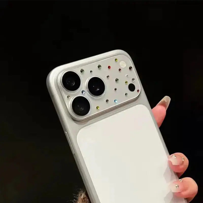 White iPhone in hand displaying the installed silver-white diamond camera lens casing with colored gemstone accents